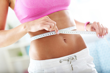 Slim young woman measuring her waist with a tape measure