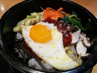 Classic Korea food vegetable Bibimbap hot stone pot, rice carrot, spinach, mushroom, cucumber, seaweed, fried egg and hot spicy chili sauce, focus-on-foreground and blur background, Asian meal
