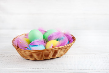 Colored eggs with feathers in basket. Concept Happy Easter.