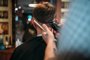 Barber hands makes hairstyle of client by clipper