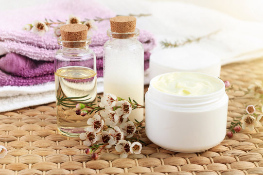 Aroma botanical spa treatment. Bottle of essential oil with flowers, jar of facial moisturizer, towels, sunlight. 