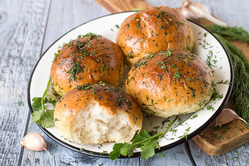 
Homemade buns.   Fresh homemade buns with garlic and greens on a white metal dish, near a sprig of dill on a kitchen cutting board.