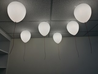LED white creamy balloons burning fly away in the sky at night in the office room with blur white wall background, holiday celebration decoration