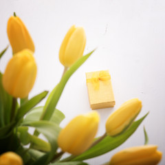 Fresh yellow tulips and golden gift box on white wooden table