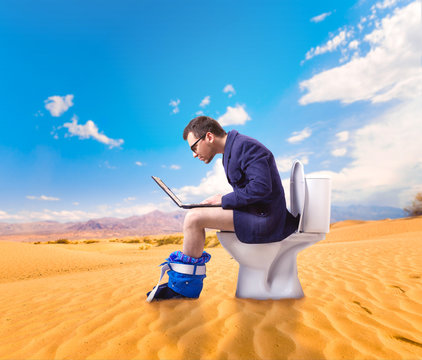 Man with laptop sitting on toilet bowl in desert