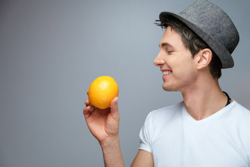A young guy with an orange in his hand wearing a hat