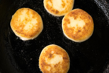 Pancakes made of cheese in a black frying pan. Pancakes curd. Pancakes fritters, a traditional dish of Russia and Ukraine.