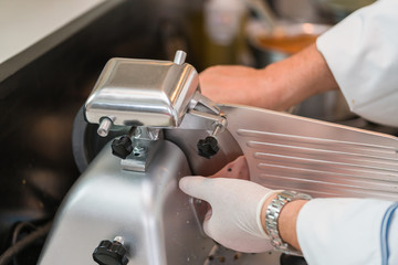 chef wearing rubber glove  using ham slicer machine
