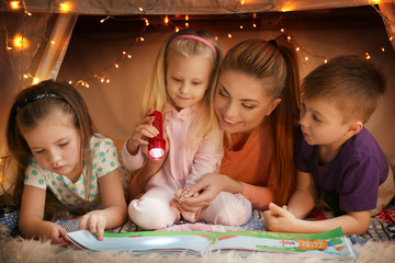 Young woman and cute children reading book in hovel at home