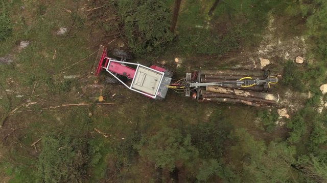 AERIAL, CLOSE UP: Timberjack harvester with loaded trailer transporting felled and stacked logs to the sawmill to be cut. Transportation of collected tree trunks from the timberland to the lumber mill