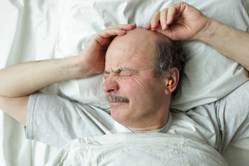 An elderly man with a mustache does not want to get up in the morning, he wrinkles his face,...