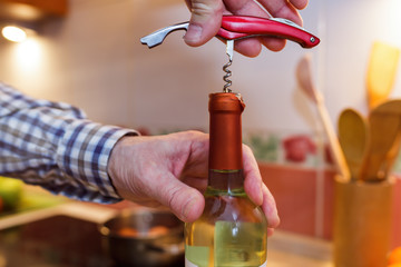 A man opens a bottle of white wine with a corkscrew