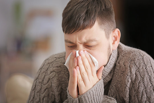 Young ill man blowing nose at home