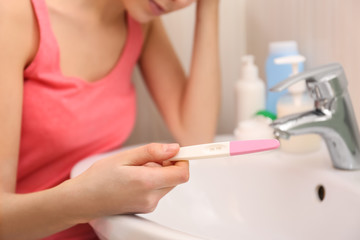 Naklejka premium Young woman with pregnancy test near sink in bathroom, closeup