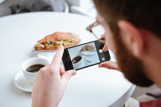Side view of a man taking photo of his food in cafe
