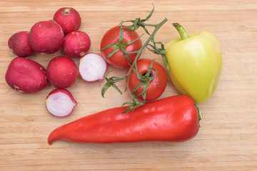 Red fresh radish, tomato, green and red pepper on wooden kitchen board