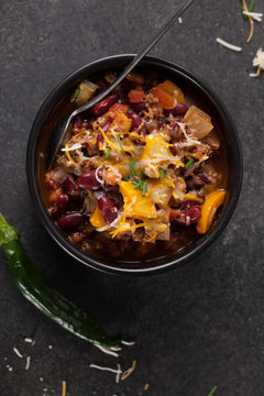 Kidney Bean Chili with tomato chunks and onion topped with cheese in large black bowl above shot