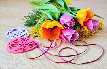 Tulips, mimosa and Easter decorations on wooden background. 