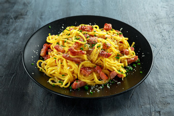 Classic Homemade Pasta carbonara Italian with Bacon, eggs, Parmesan Cheese on black plate.