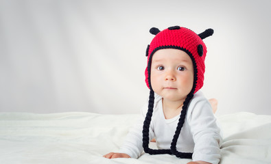 Cute baby lying in the bed on white blanket in ladybug hat