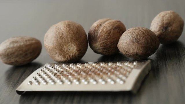Slow pan on mini grinder and Myristica fragrans pieces shallow DOF 4K 2160p 30fps UltraHD footage - Assorted nutmeg fruit spice on wooden table 3840X2160 UHD panning video 