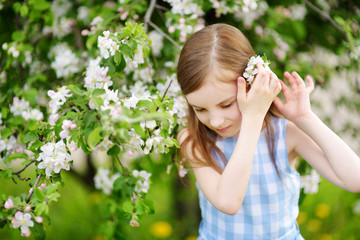 Obraz premium Adorable little girl in blooming apple tree garden on beautiful spring day
