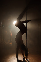 Young sexy woman exercise pole dance on a dark background