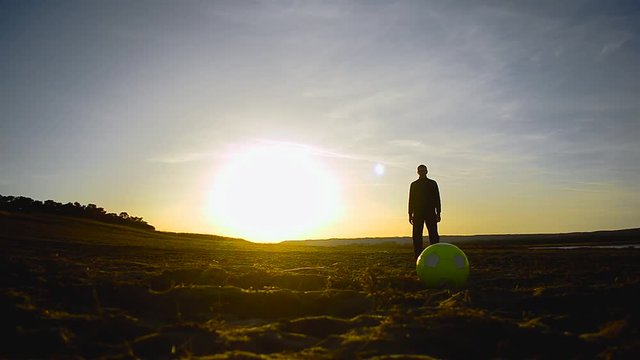 silhouette of man with ball standing on the beach lit by sun
