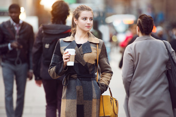 Young adult businesswoman walking on city street to the work in the group of multicultural people. Woman holding coffee cup and looking to the side.