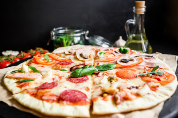 Pizza with ingredients, spices and cutlery on black background. Tasty pizza.