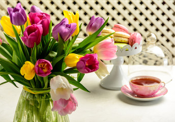 Beautiful festive bouquet of tulips, cakes and cup of tea on white background.