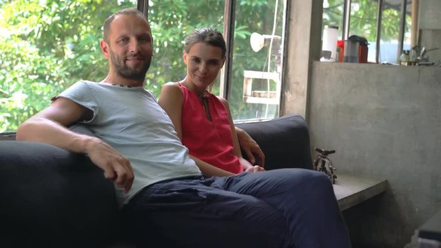 Portrait of happy couple sitting at home by the window, 4K
