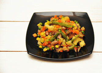 Black plate with a vegetable saute on a white wooden background