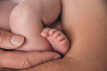 Leg of the newborn baby on the background of the hands of the father.