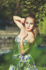 Naklejka premium Beautiful colorful toned portrait of sensual young sportive woman with emotional eyes and long hair, in floral dress, standing in park