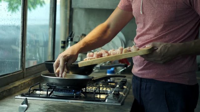 Young, handsome man cutting and putting meat on the pan,
