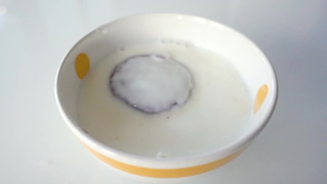 Chocolate biscuit falls in milk white cup. Footage in super slow motion.