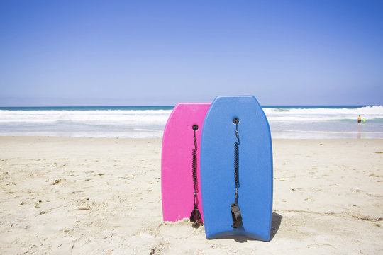 Two colorful boogie boards resting on a pristine beach. Ready to ride and have fun in the ocean on a clear summer day. Vacation time