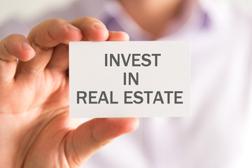 Businessman holding a card with INVEST IN REAL ESTATE message