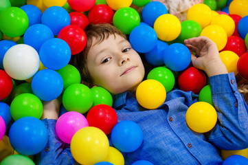Happy boy having fun in ball pit on birthday party in kids amusement park and indoor play center. Child playing with colorful balls in playground ball pool. Activity toys for little kid