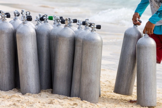 A collection of scuba divers air taks on a tropical white sand beach.