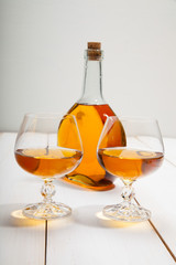 Glasses with cognac and a bottle on  white wooden background