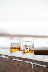 Two whiskey glasses in the snow on a winter background.