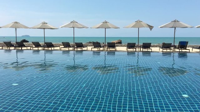 Umbrella and swimming pool in hotel resort with sea beach background. uhd 4k 3840x2160.
