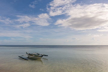 A Filipino fisherman's basic pump boat floating empty on a still calm tropical sea with seagulls resting on its stabilizers.