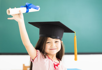 Portrait of  cute schoolgirl with graduation hat in classroom