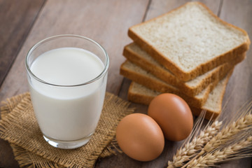 Milk glass with egg and bread on wooden table
