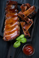 Closeup of barbecued pork ribs on a black wooden serving tray, selective focus