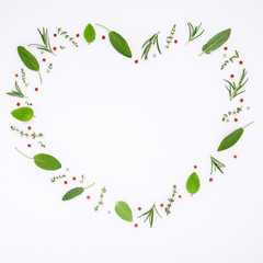 Fototapeta premium Heart shaped frame various fresh herbs rosemary, sage ,thyme and peppermint leaves flat lay with central copy space on white wooden background.
