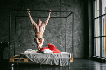 Young sexy men bodybuilder athlete,studio portrait loft on background of stylized wall,guy model With a bare torso pulls up on a horizontal bar on brutal male bed made of metal and pallets